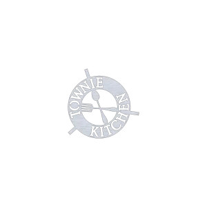Round aluminum trivet featuring the words 'Townie Kitchen' cut out in bold letters, with a fork and spoon crossing in the center. The design is sleek and functional, reflecting Newfoundland charm. Displayed against a black background.